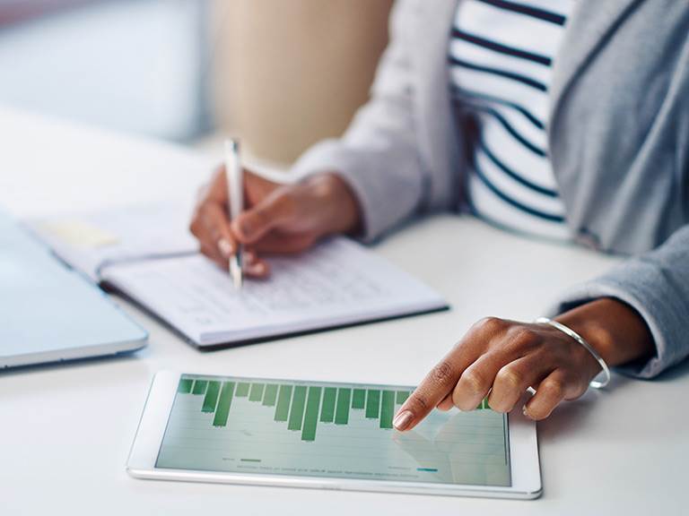 woman filling out a ledger while using a tablet