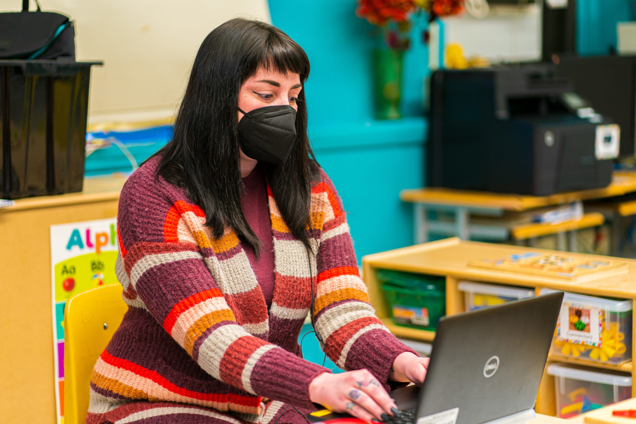 A masked teacher using a laptop